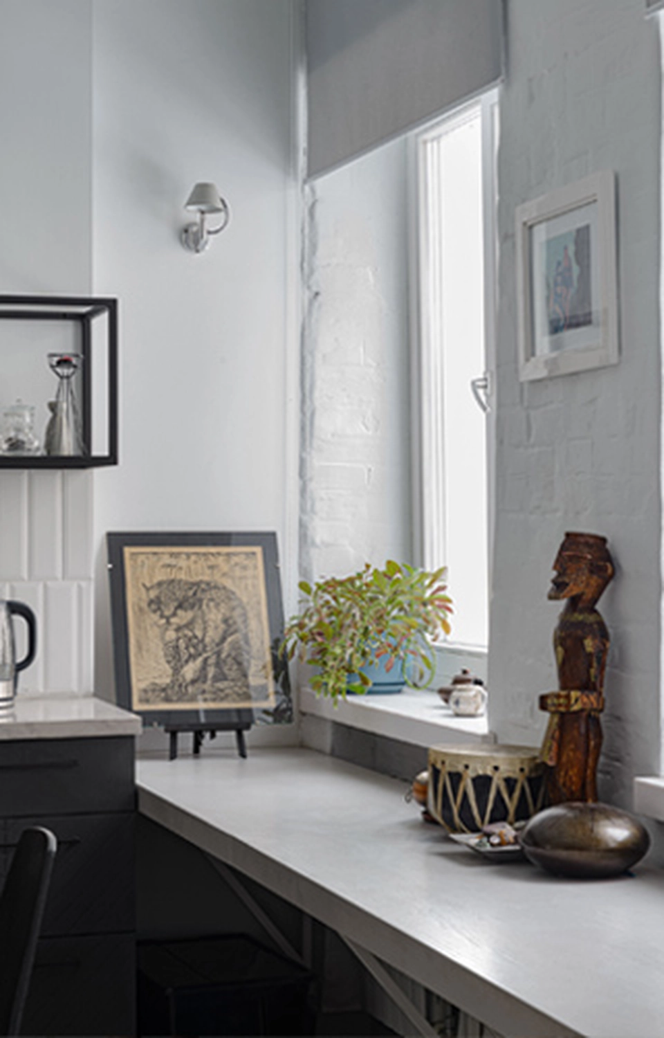 GM-Fensterbau - Fenster - Türen - Rollladen - Ein modernes weißes Interieur mit einer langen Arbeitsplatte aus Beton entlang einer mit Pflanzen geschmückten Fensterbank, einem gerahmten Bild und rustikalen Holzartefakten.